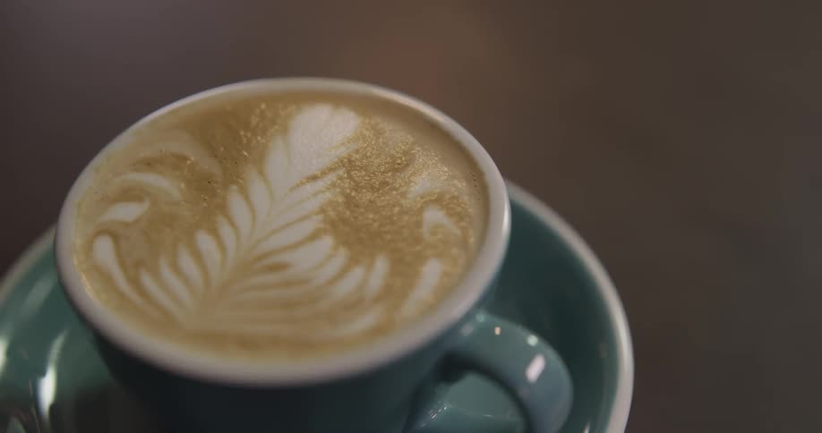 A person picks up a cup with a design on the top of a latte
