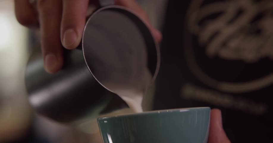 Barista creating latte art while pouring milk in a blue cup