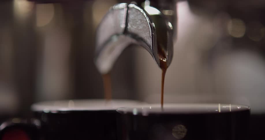 Coffee drips out of a machine and in to two mugs