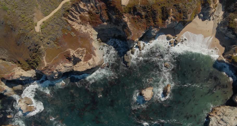 Ocean waves break and splash against the rocks and the small sandy beach