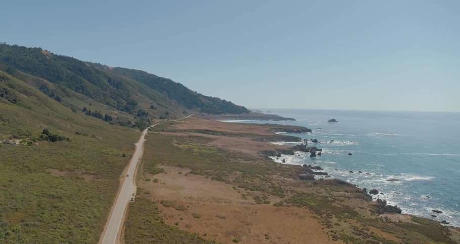A rocky shore with a road and hills in the background