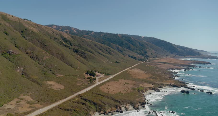 A narrow road sits at the bottom of a mountain range next to the sea