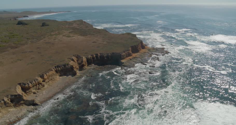 The ocean water rolls into shore near the hills