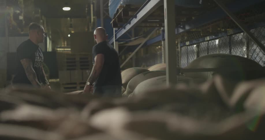 Two men carry a sack in a warehouse
