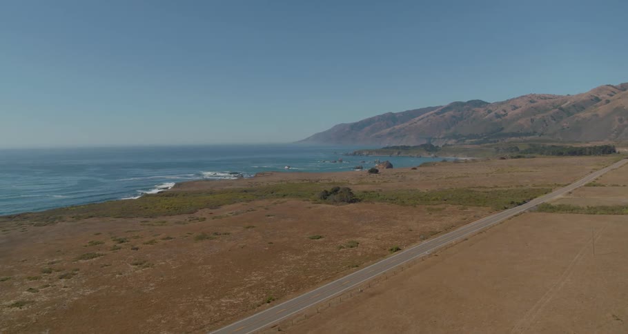 An empty road stretches along the ocean coast towards the hills