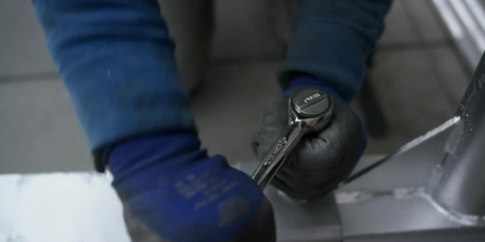 Hands covered by blue gloves tightening a bolt with a wrench