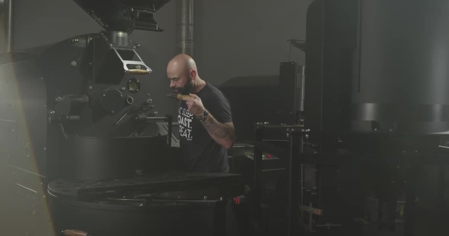 A bald man examining and blowing on a part from a large black machine