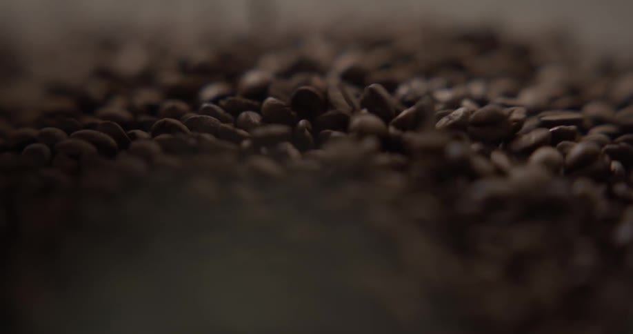 A large quantity of coffee beans are being poured atop a pile of beans that were already there
