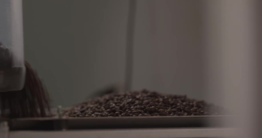 A tattooed man pouring coffee beans from a plastic tub into a metal container on a machine