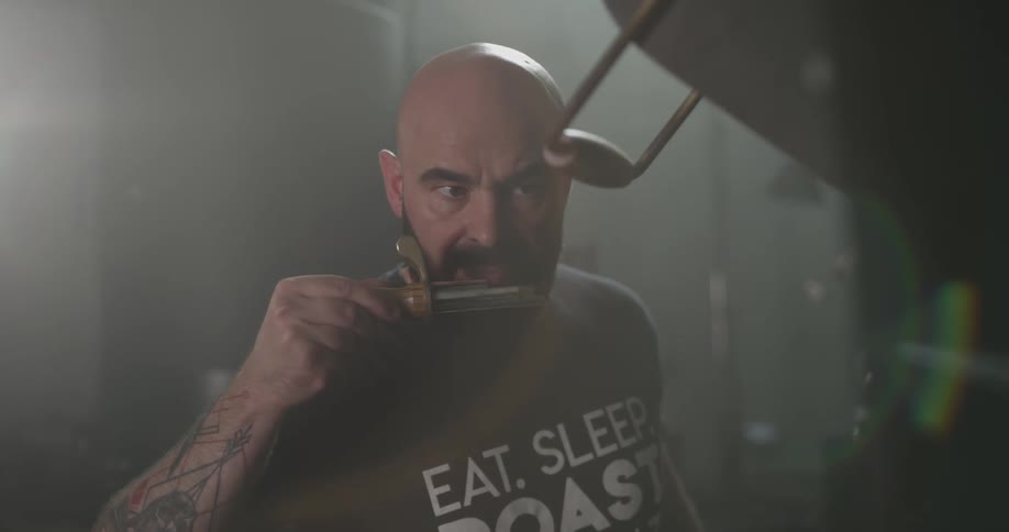 A bald man removes a device from a coffee roasting machine and smells it before placing it back into the machine