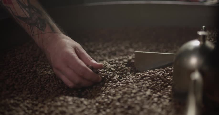A man grabs a handful of coffee beans from a mixer