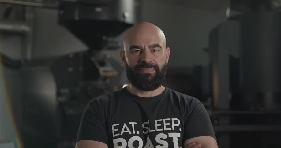 A man with a beard standing in front of a coffee roasting machine