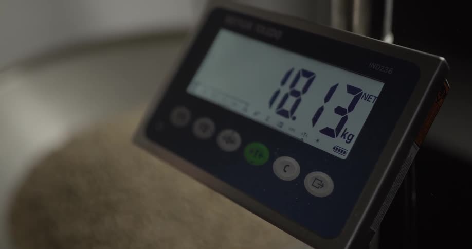 The numbers increase on the digital scale as someone scoops something in the container