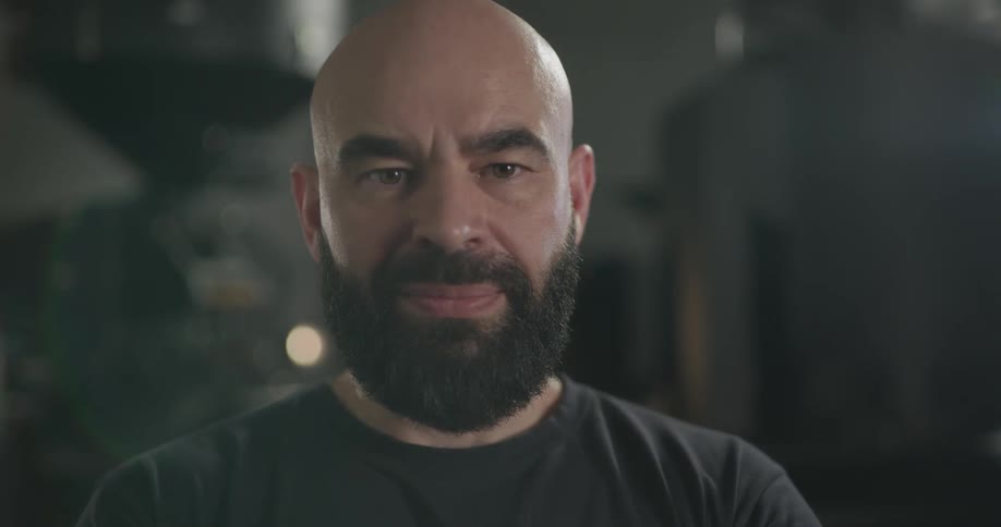 A bald bearded man lifting his head to look into the camera