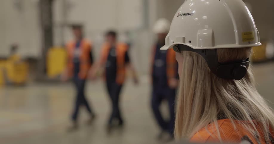 A blonde woman in a hard hat waves at three coworkers