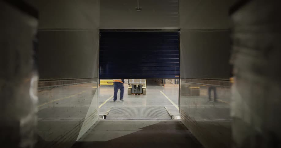 A door opens in to a warehouse where a man is about to drive a loader
