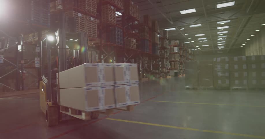 A forklift drives by with a cardboard box on a pallet in a warehouse