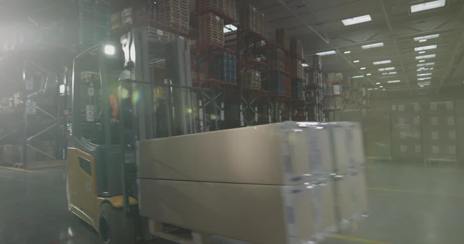 A man moves boxes through a warehouse with a forklift