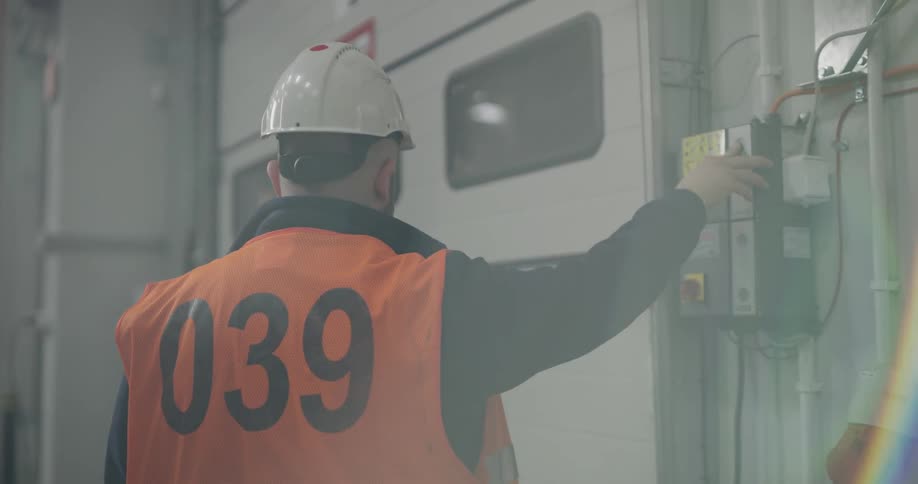 A man with a hardhat and orange vest pressing a button to open a door