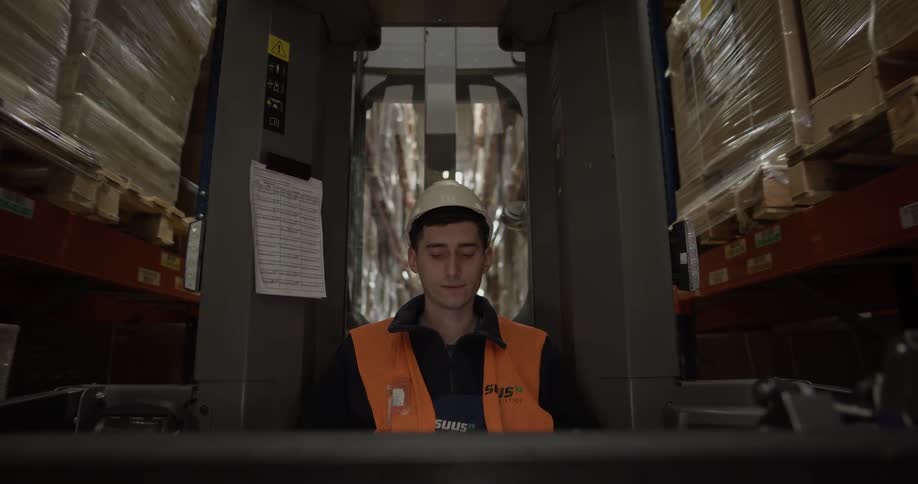 A warehouse worker drives a forklift back and forth down an aisle