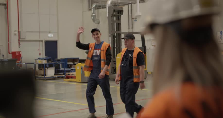 Employees wearing orange vest walking by and waving in a warehouse