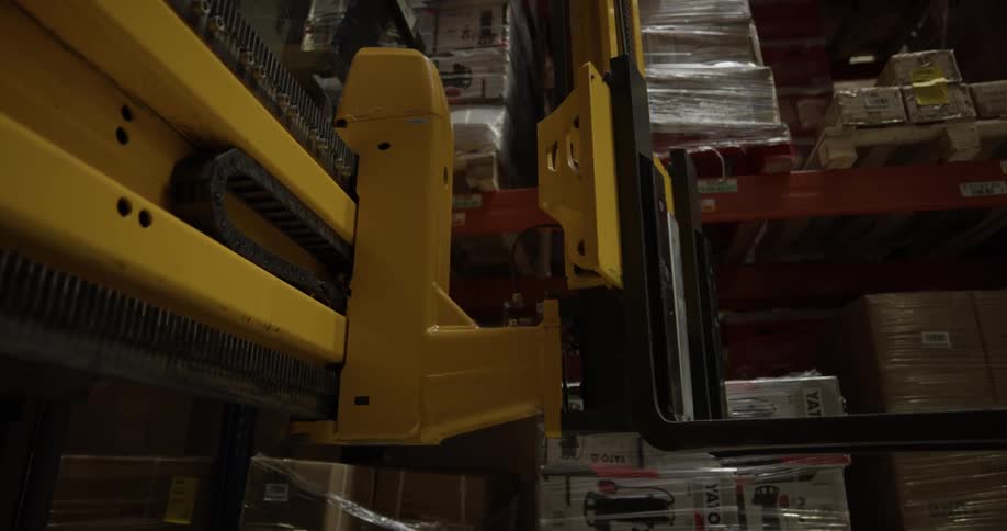 A forklift turns toward a shelf in a warehouse