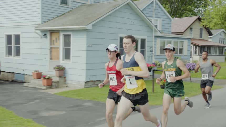 A small group of men wearing numbers run past homes as they participate in a road race