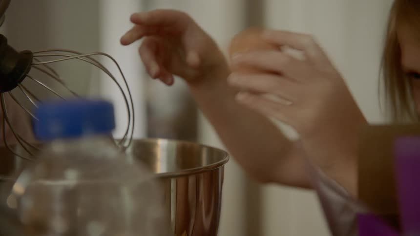 A little girl cracks an egg in to a mixing bowl