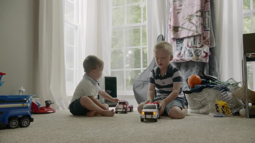 Two young boys play with trucks on the carpet