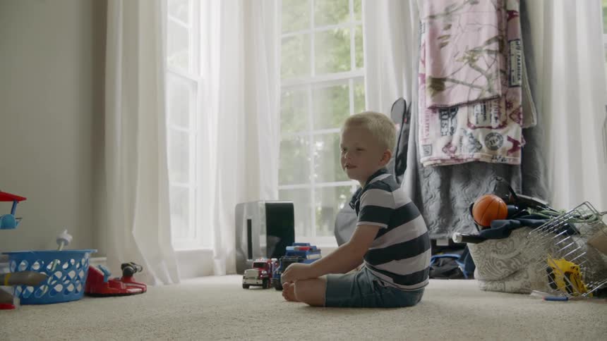 A young caucasian boy plays with trucks as he sits on the ground until he jumps up to join another boy