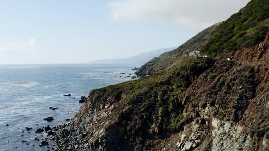Vehicles driving along a road above the rocky coastline