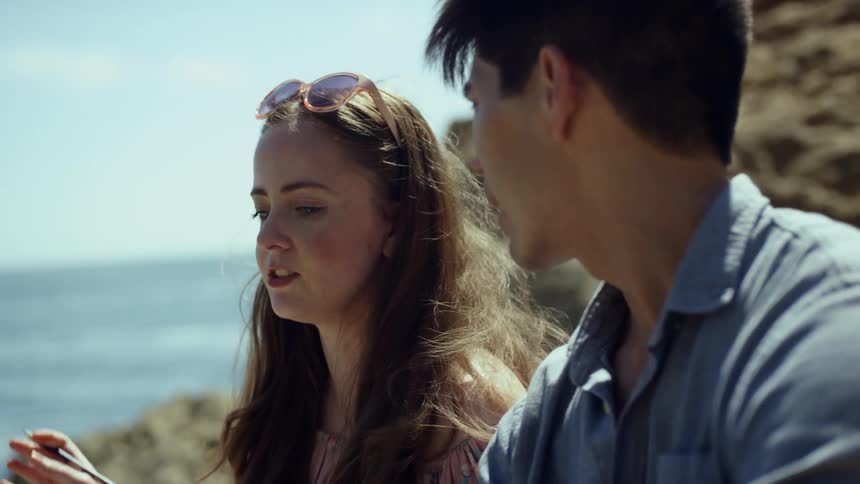 A man and woman talk while sitting on rocks at the edge of the sea