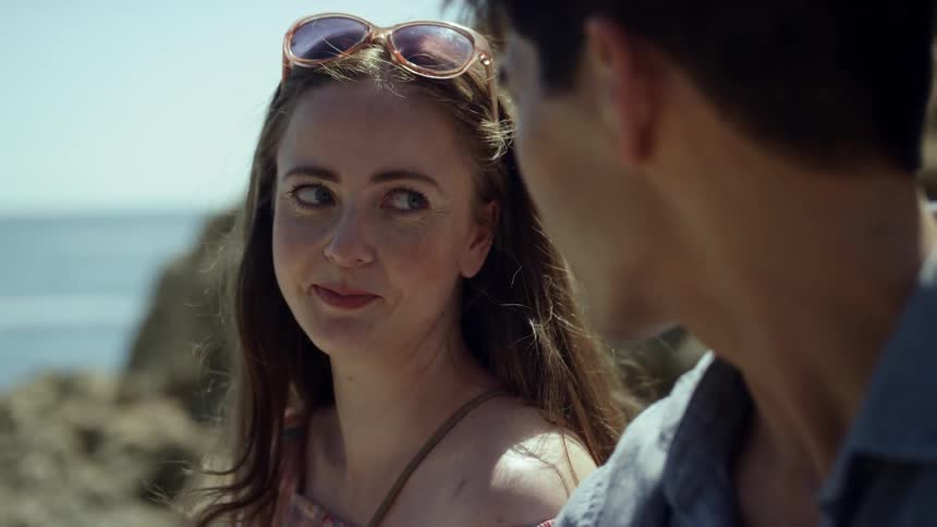 A man and woman smile while looking adoringly at each other outside on a sunny day