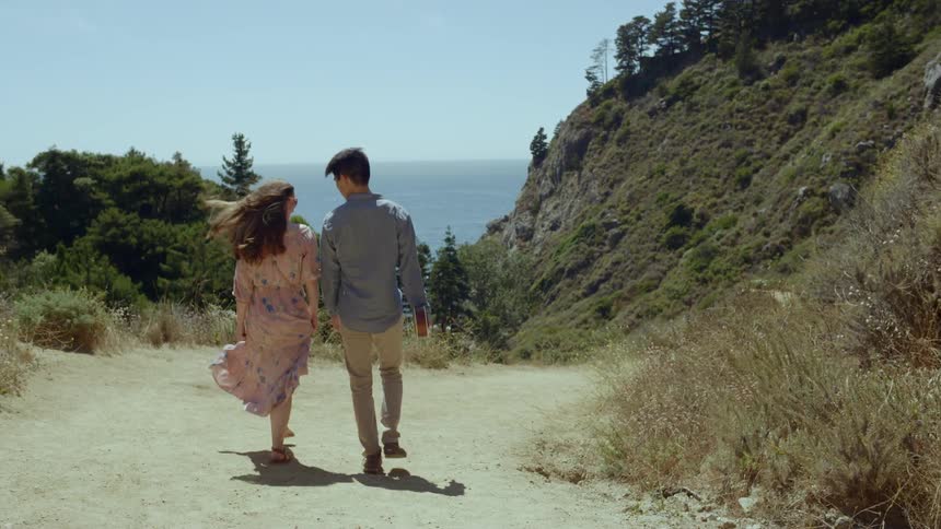 A couple walks hand in hand on a sandy trail on a sunny and windy day