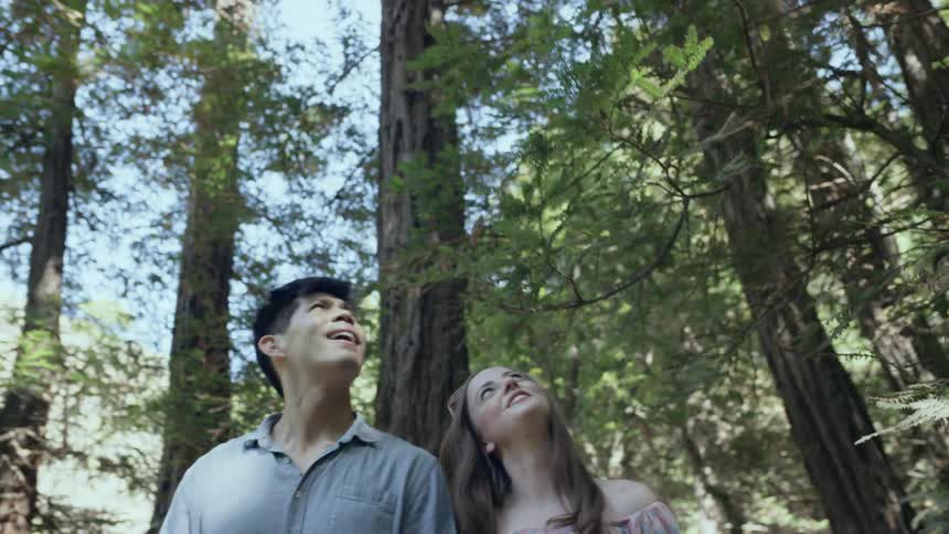 A man and woman are walking through a forest area