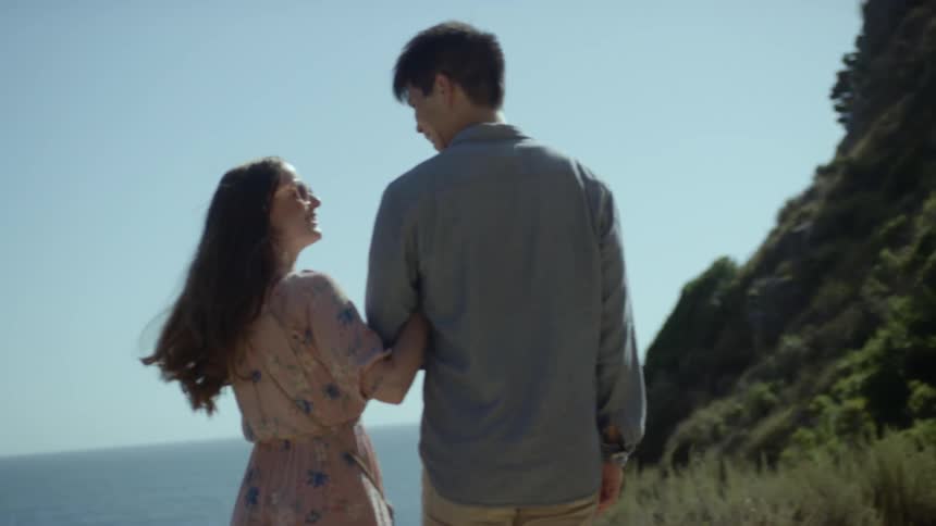 Asian man and white woman stand on a cliff and look at the sea during daylight
