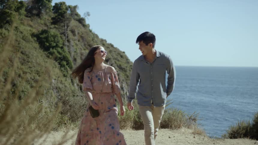Two people walking down a path by the ocean