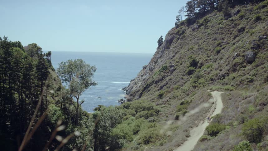 People walk on a hillside dirt road on the coast