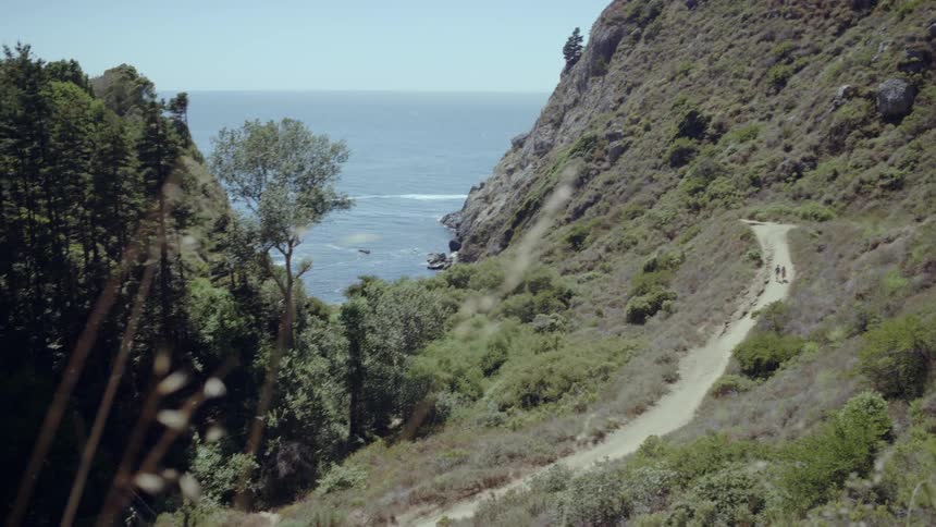 A wide shot of two people walking down a path by the ocean