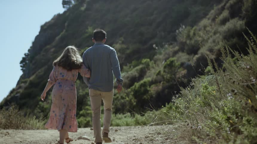 A woman holding a mans arm while walking on a dirt road