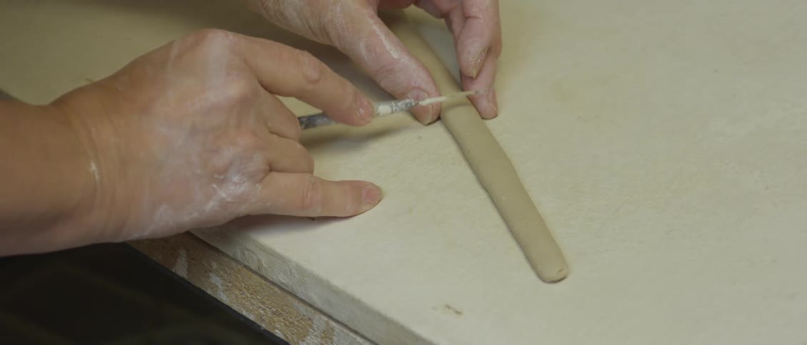 Someone slices off a piece of a tube of clay