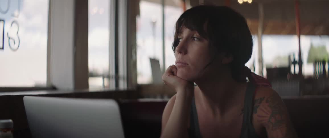 A woman sits at a restaurant table with a laptop in front of her