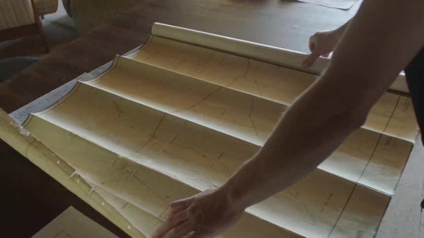 Man unrolls old map on table inside house