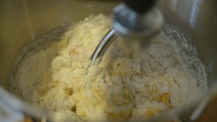 A dough hook mixes flour and eggs in a stainless bowl