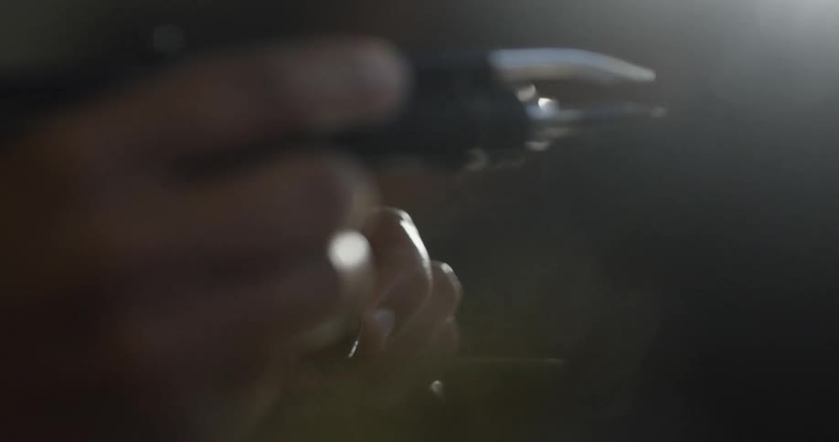 Smoke rises from a soldering iron as a mans hands move it away from a piece of metal