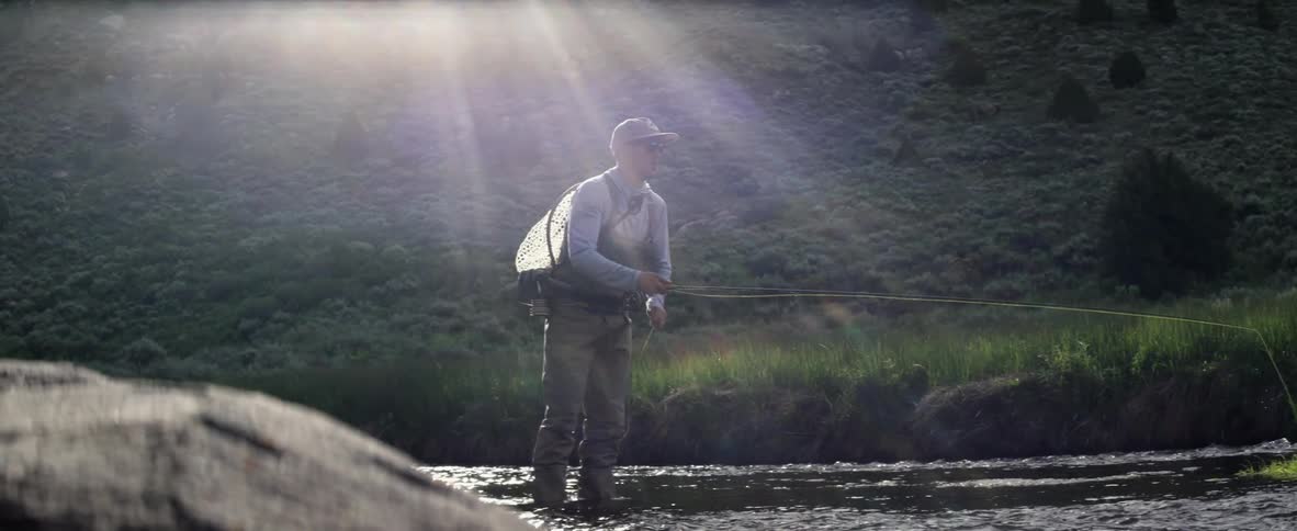 Sunbeams shining down on a man fly fishing