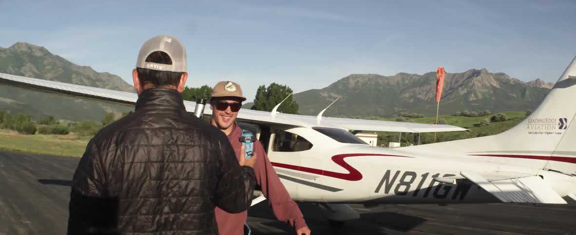 Two men greet each other near a small airplane
