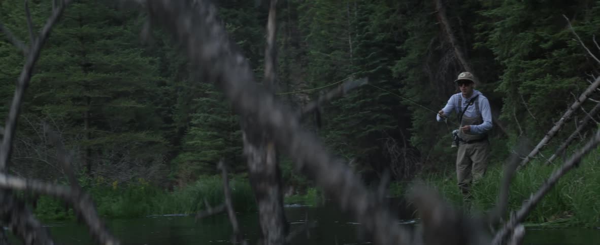 Man stands at the edge of a river fly fishing