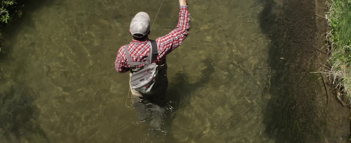A fly fisherman fishes in a stream on a sunny day
