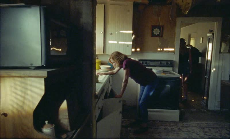 A woman is leaning over the kitchen sink as younger female listening wearing headphones walks past and leaves the room